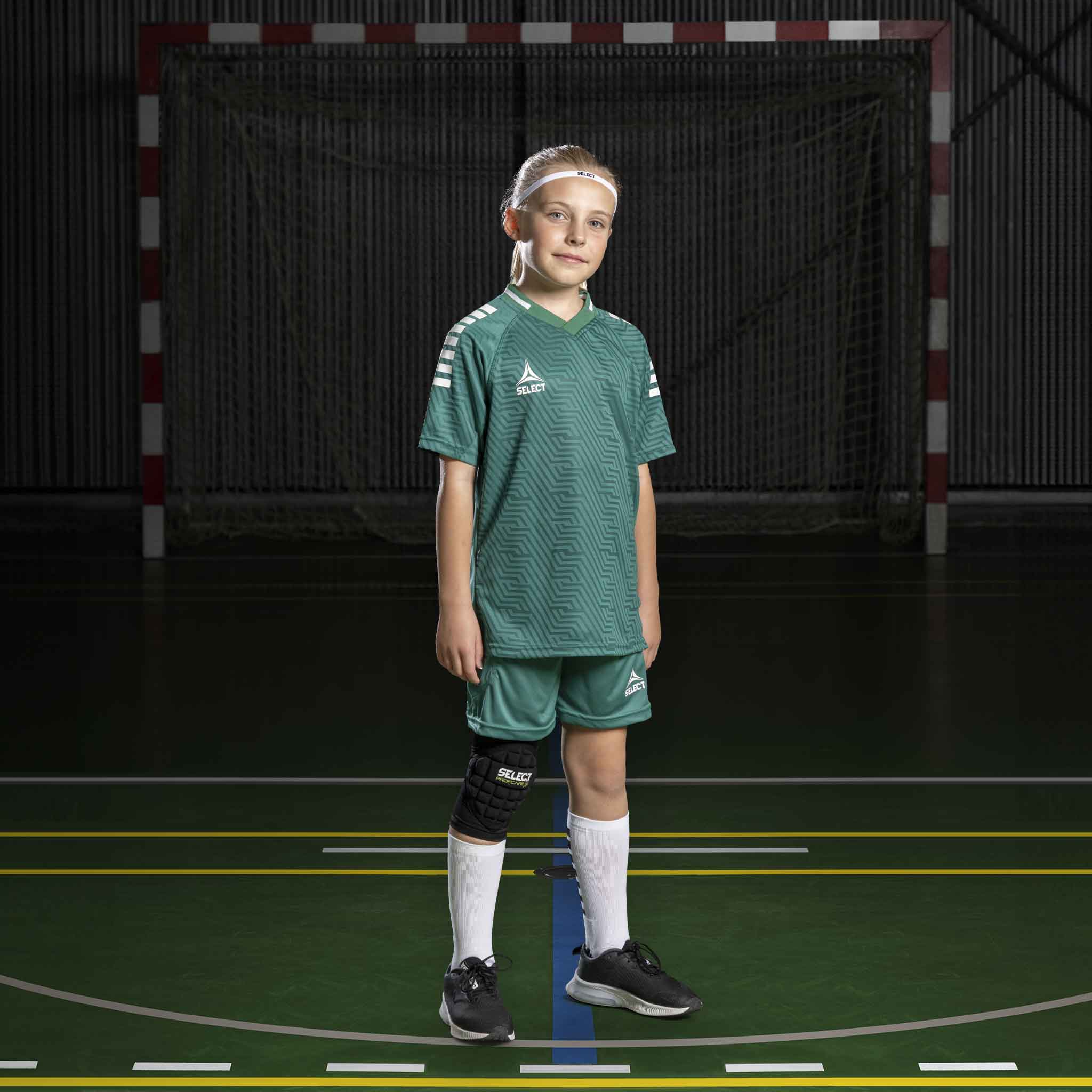 Gutt fotballspiller i grønn-hvite Player shorts Monaco v24, Match & Training wear, sett forfra på innendørs bane.
