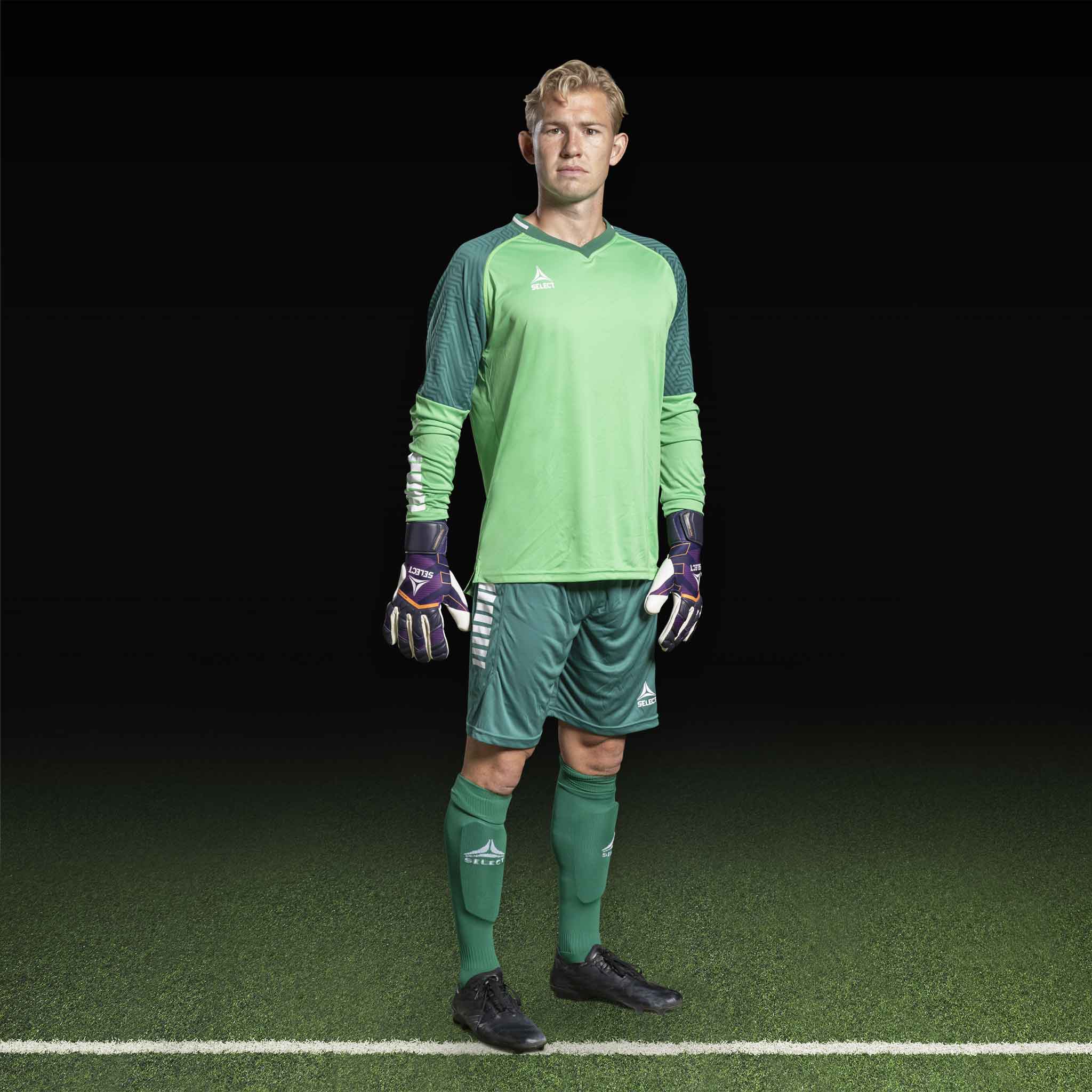 Mannlig fotballspiller i grønn Goalkeeper shirt Monaco v24, keeperklær, sett forfra med hansker på banen.
