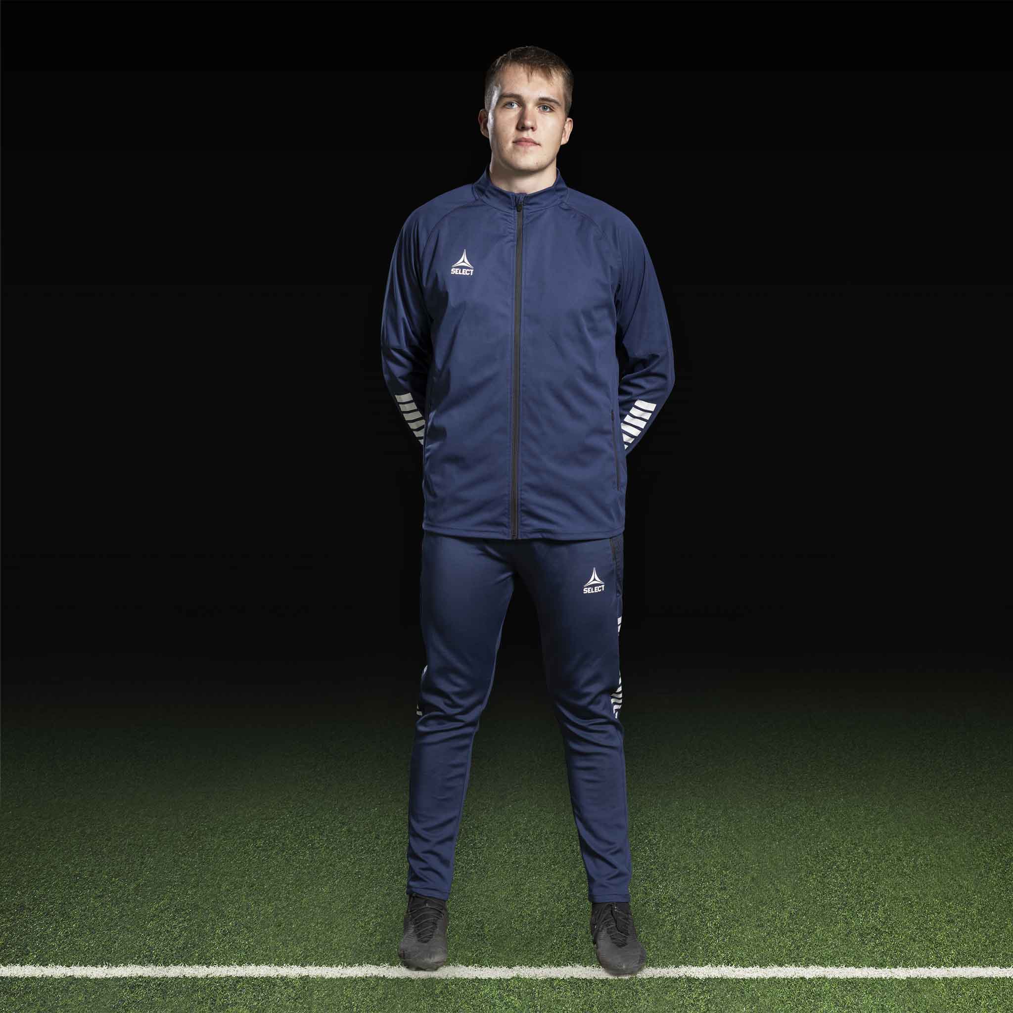 Mannlig fotballspiller i marineblå Training jacket Monaco v24, Match & Training wear, med hvit logo, forfra på banen.