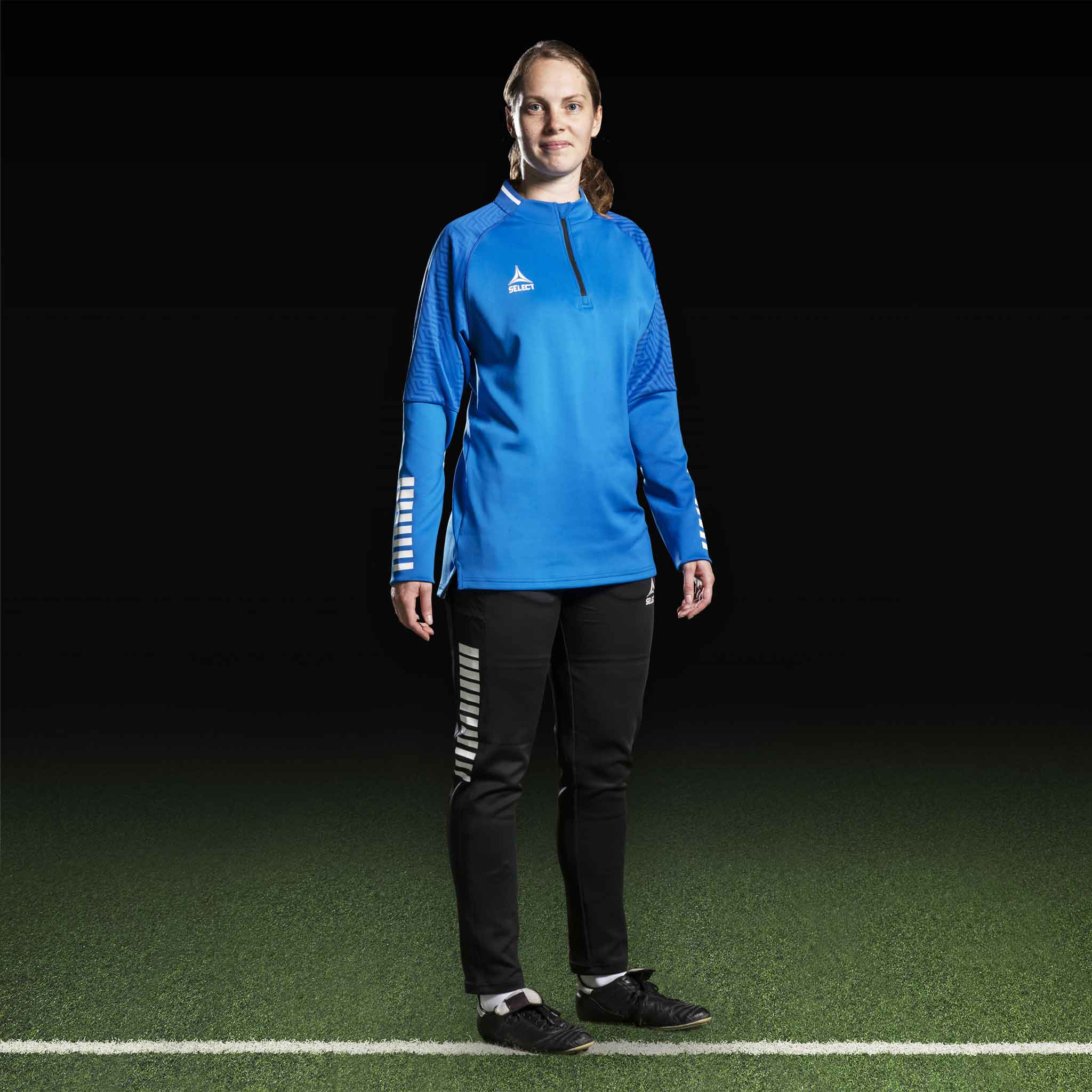 Kvinnelig fotballspiller i blå Training sweat 1/2 zip Monaco v24, Match & Training wear, med sorte bukser, sett forfra.