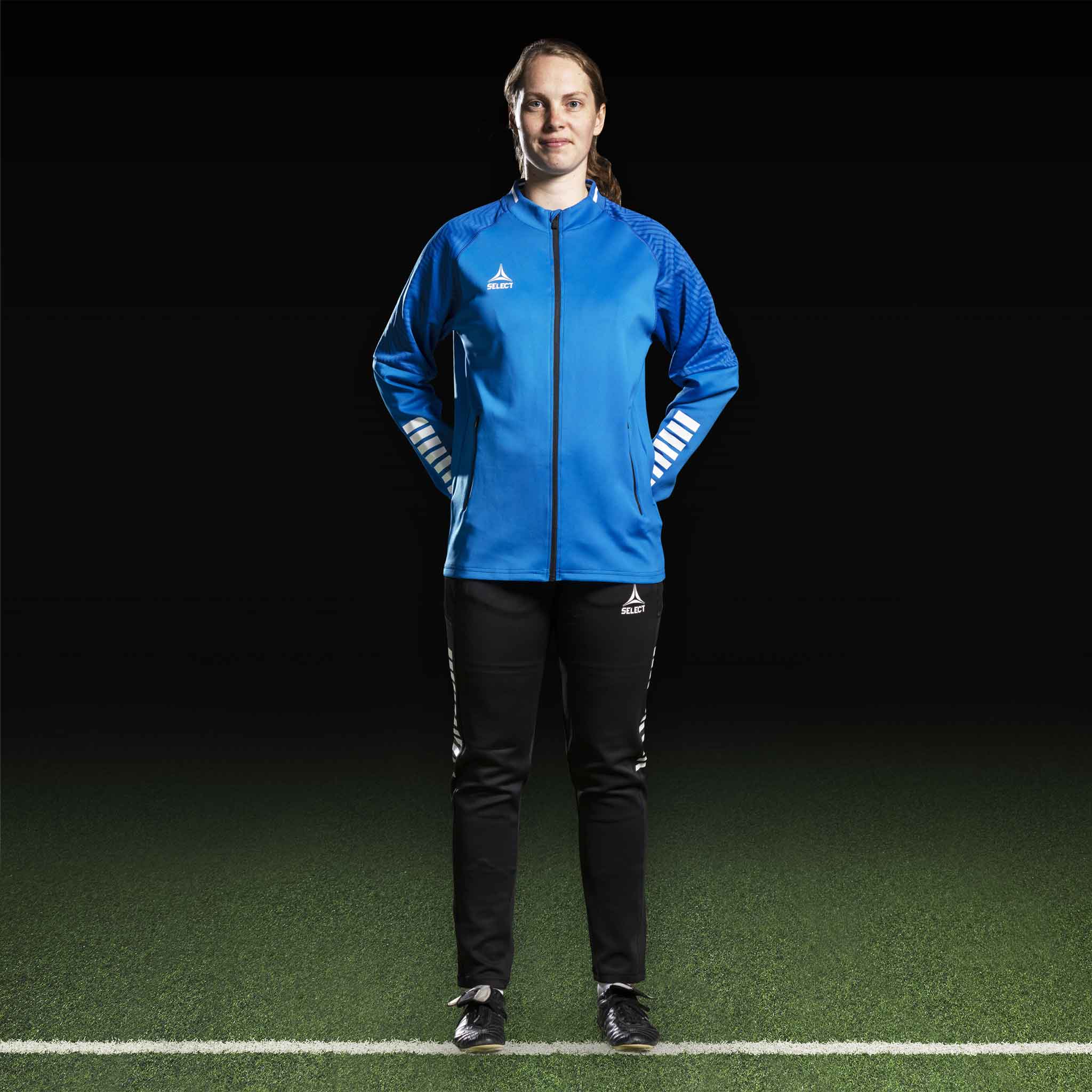 Kvinnelig fotballspiller i blå Zip jacket Monaco v24 og sorte bukser, Match & Training wear, sett forfra.
