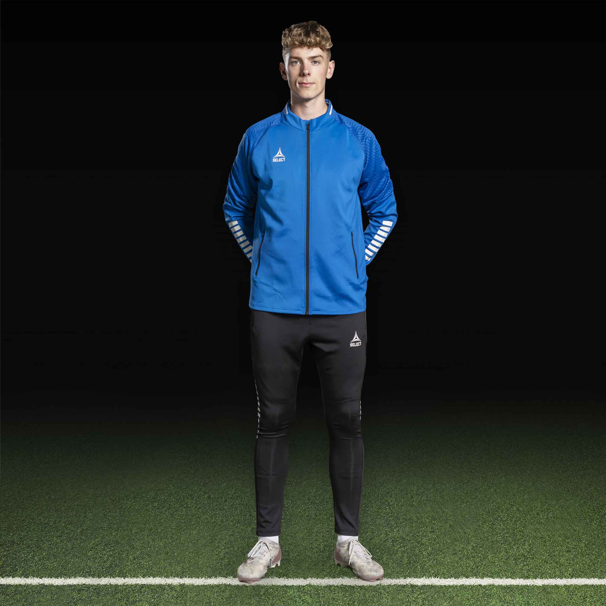 Mannlig fotballspiller i blå/hvit Zip jacket Monaco v24 og svarte bukser, Match & Training wear.