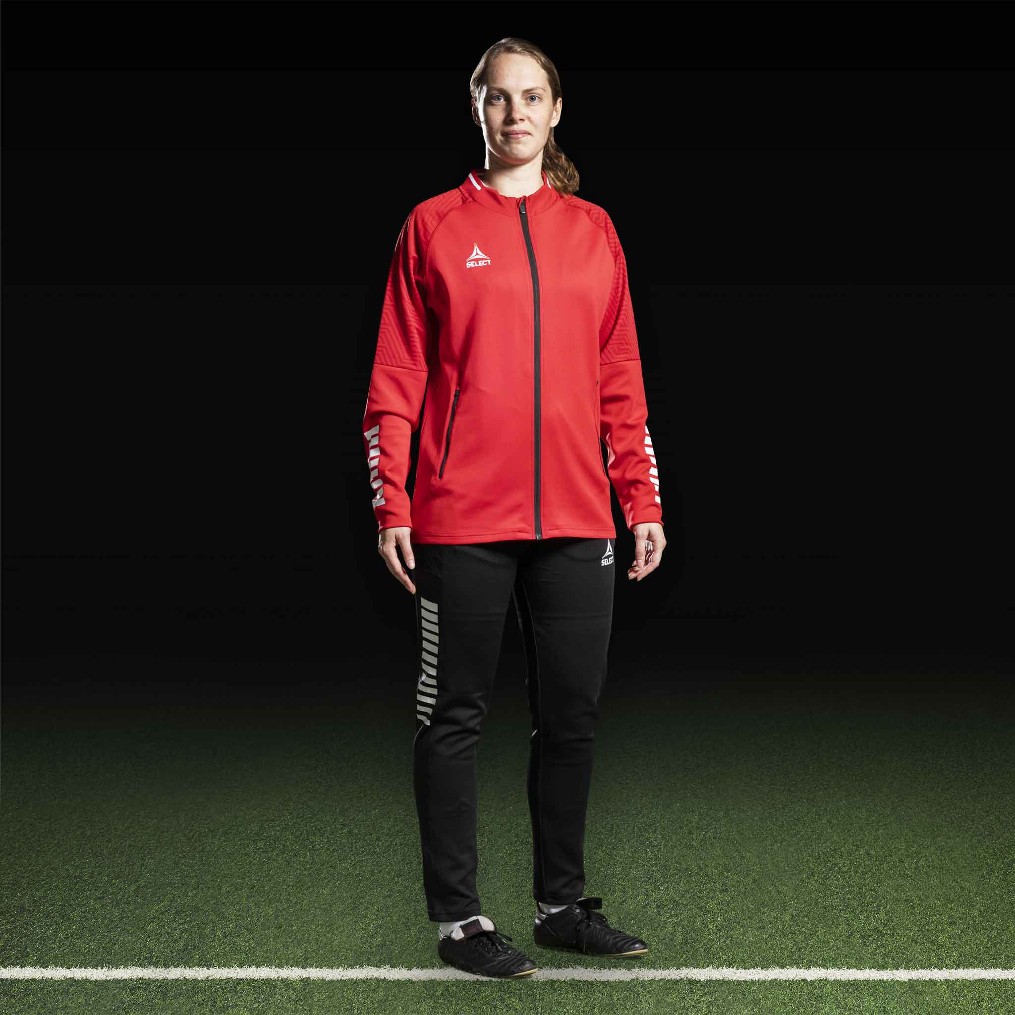 Kvinnelig fotballspiller i rød Zip jacket Monaco v24 og svarte bukser, Match & Training wear, sett forfra.