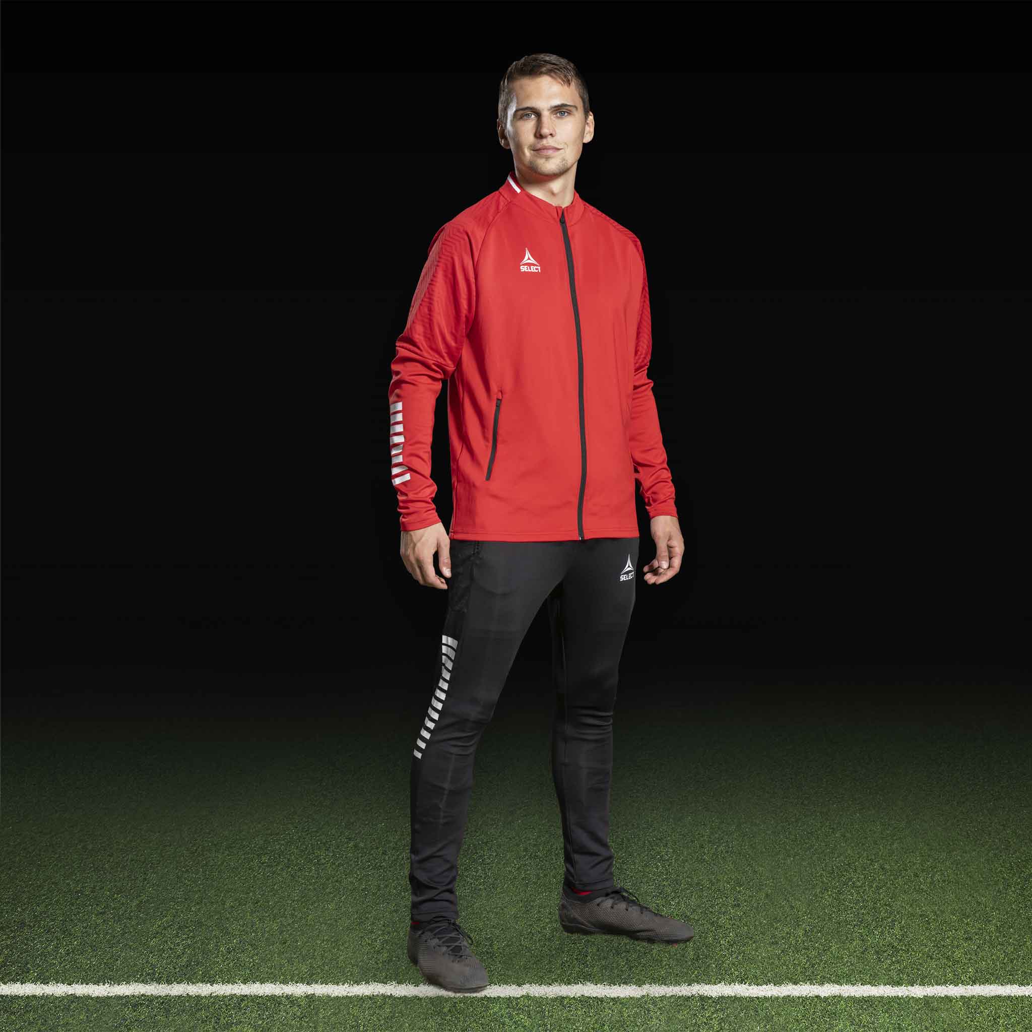 Mannlig fotballspiller i rød Zip jacket Monaco v24 og svarte slim fit-bukser, Match & Training wear.