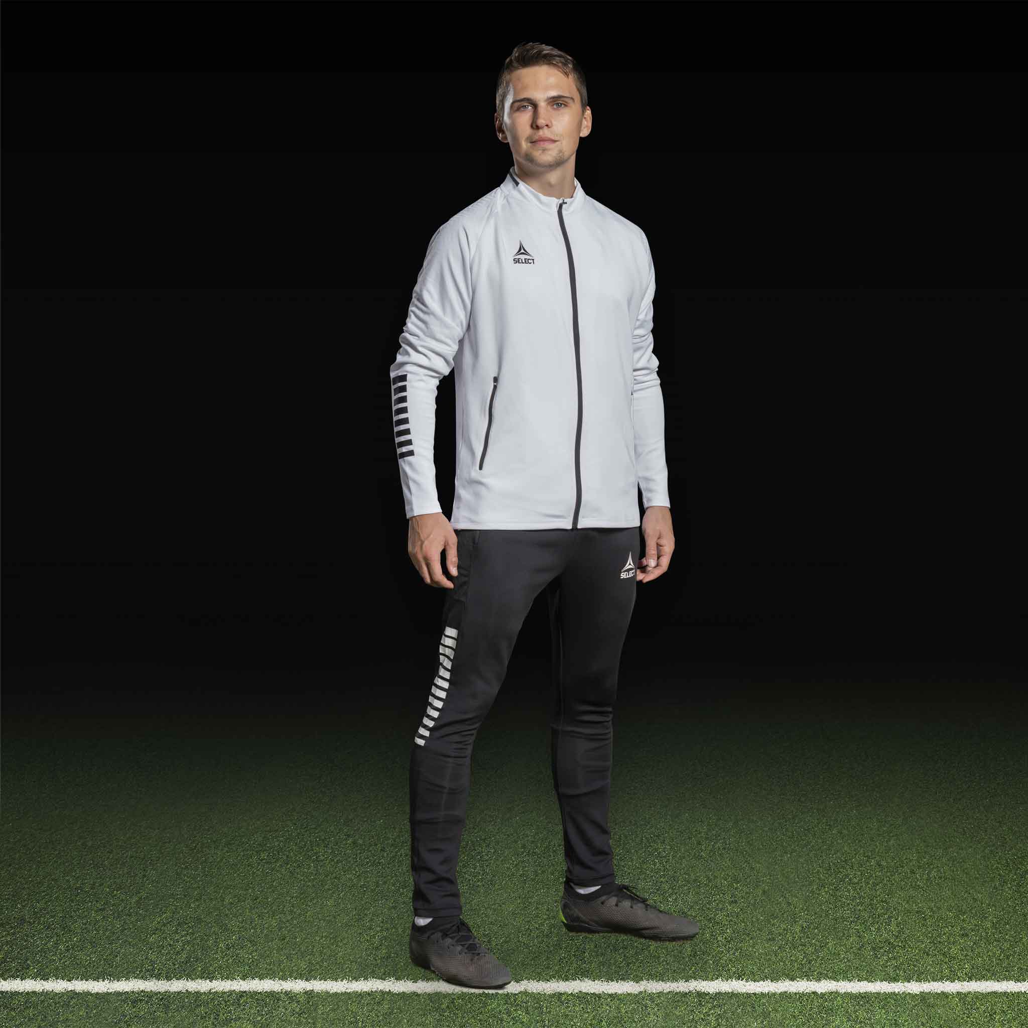 Mannlig fotballspiller i hvit Zip jacket Monaco v24 og sorte bukser, Match & Training wear.
