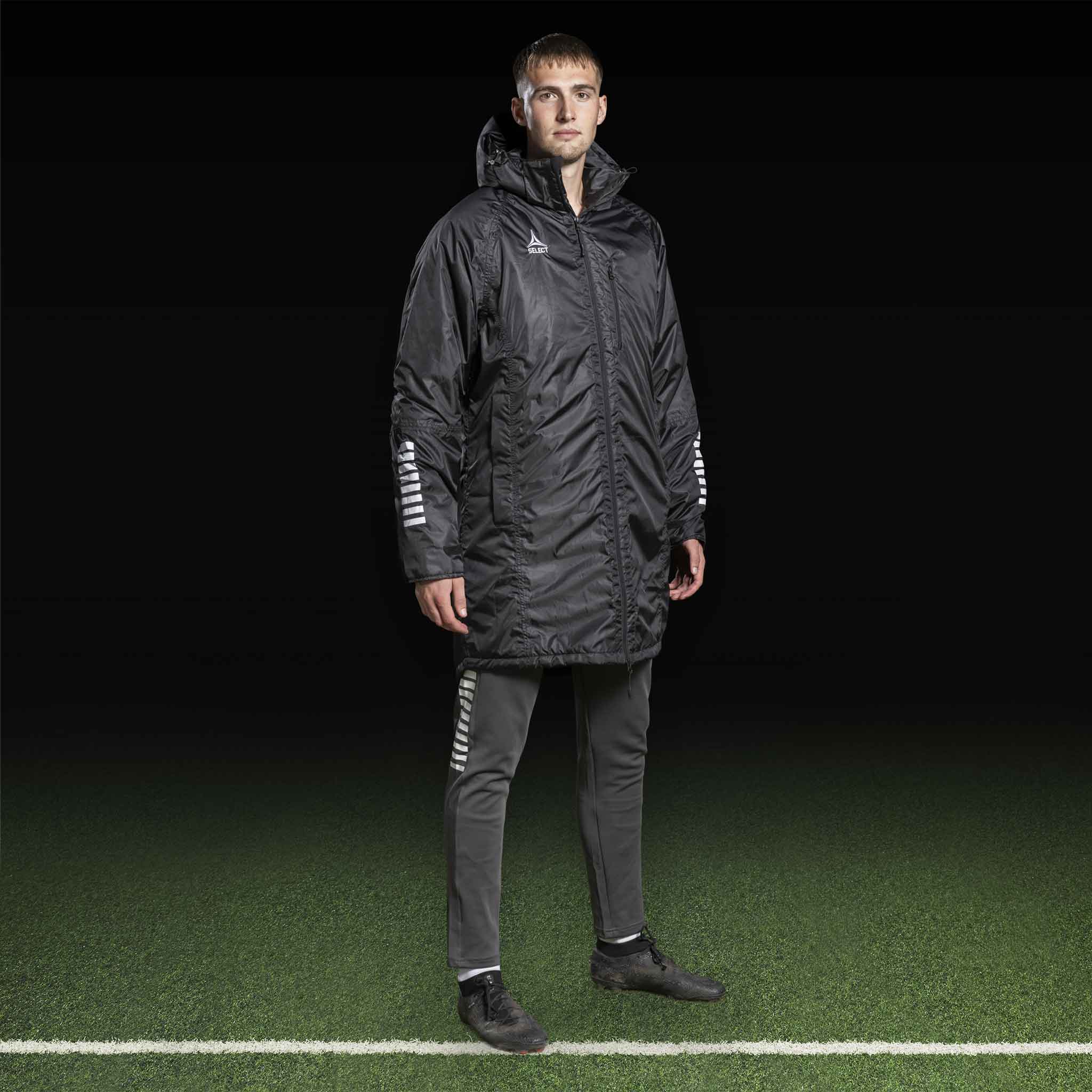 Mannlig fotballspiller i sort Coach jacket Monaco v24 med grå bukser, Match & Training-tøy.
