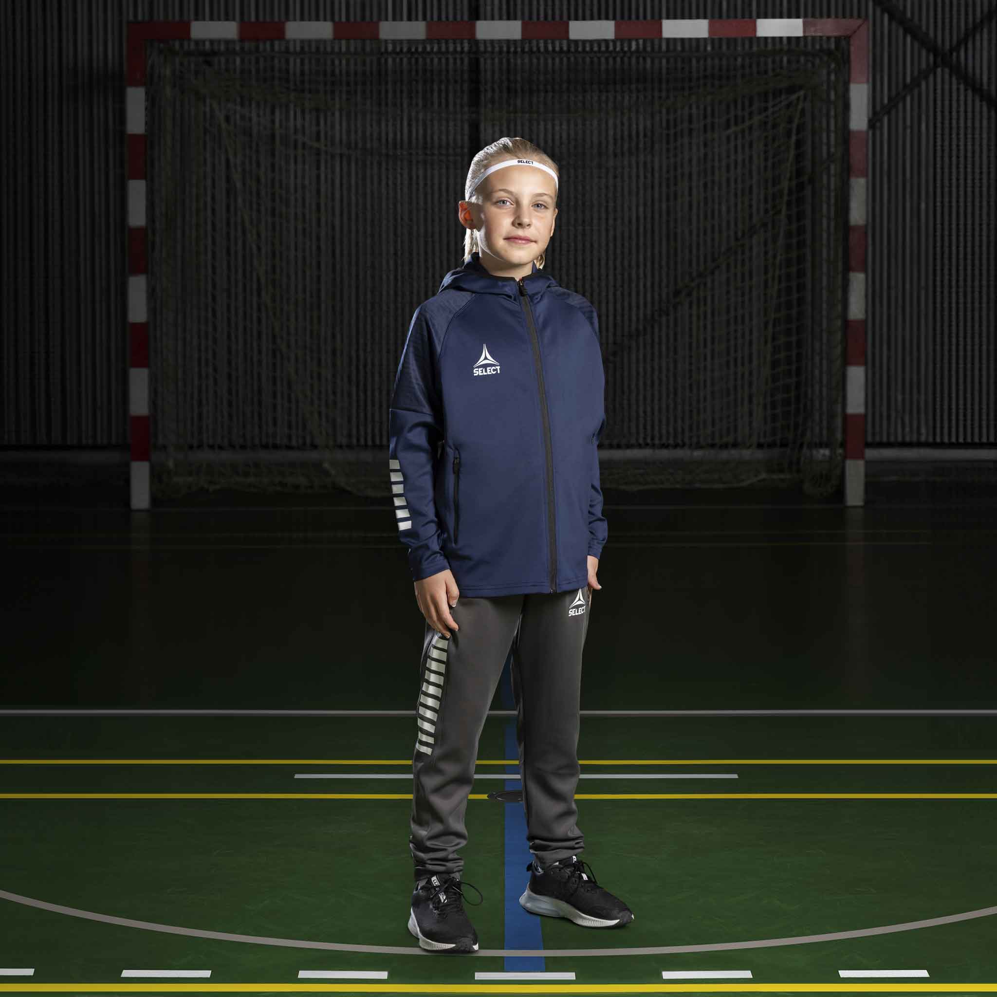 Håndballgutt i marine/hvit Zip hoodie Monaco v24 og grå bukser, Match & Training wear, på banen.