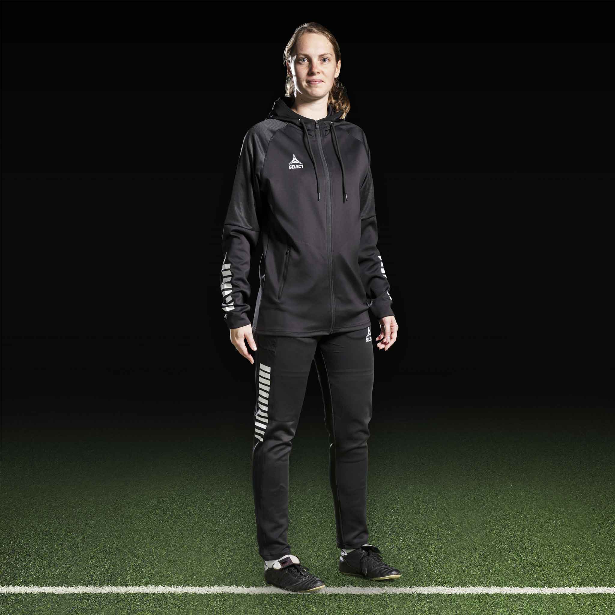 Kvinnelig fotballspiller i sort-hvit Zip hoodie Monaco v24, Match & Training wear, forfra på banen.