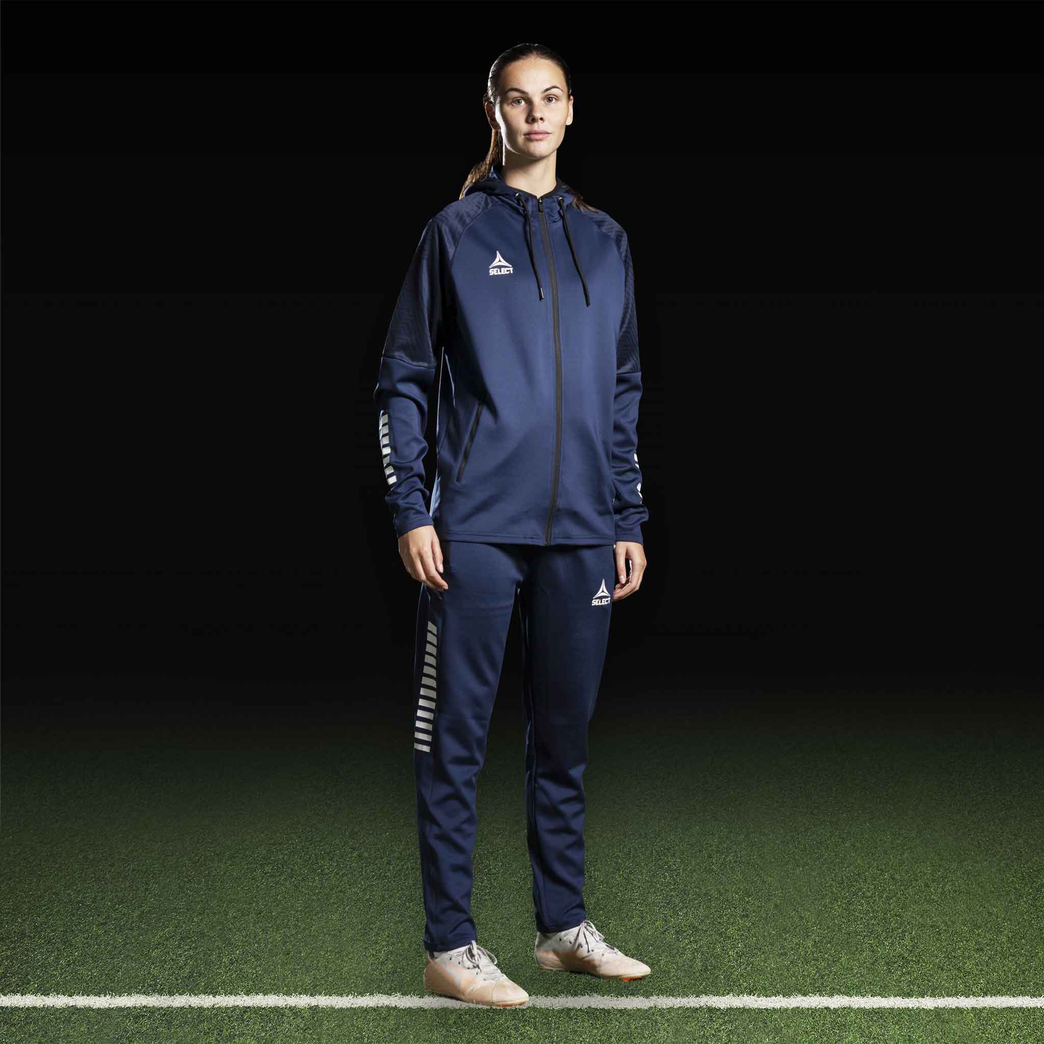 Kvinnelig fotballspiller i marineblå Zip hoodie Monaco v24, Match & Training wear, forfra med hvite logodetaljer.