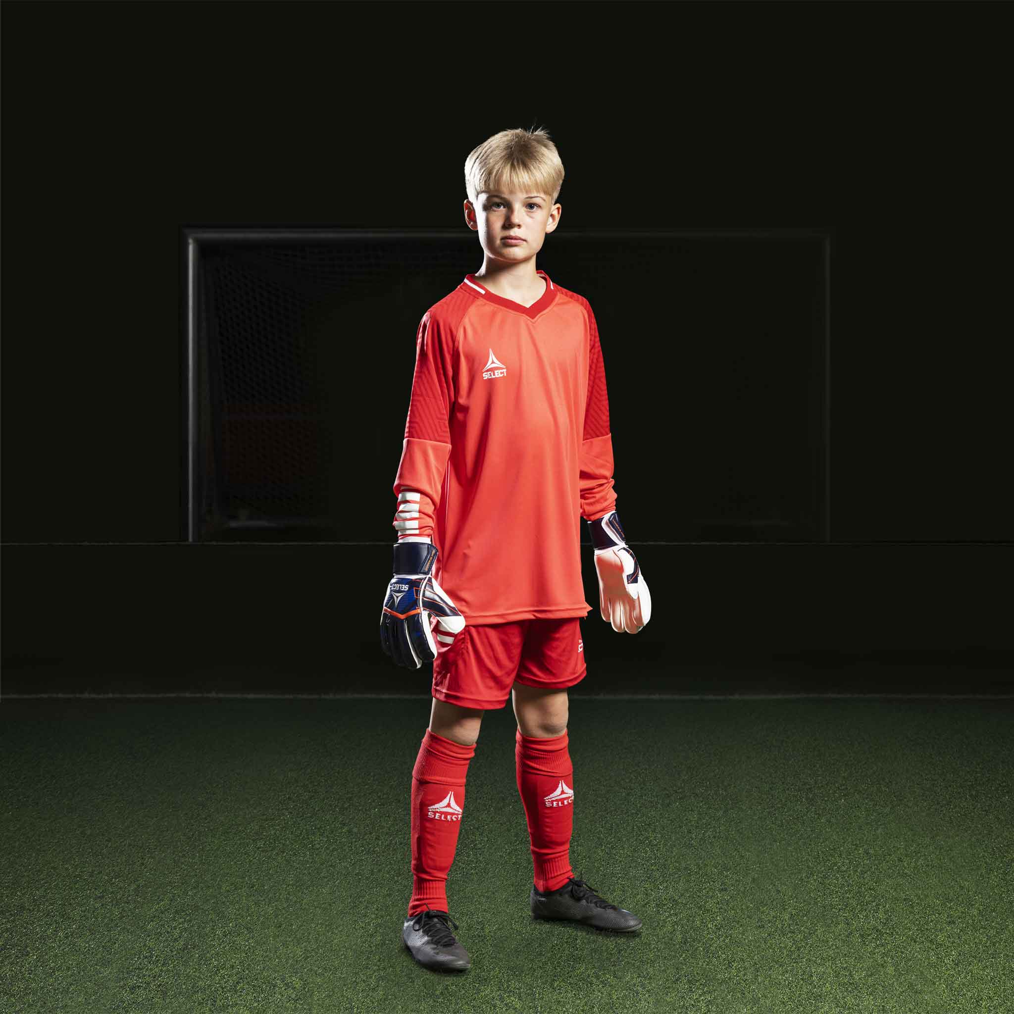 Gutt fotballspiller i rød Goalkeeper shirt Monaco v24, målvaktsklær, med matchende shorts og strømper.