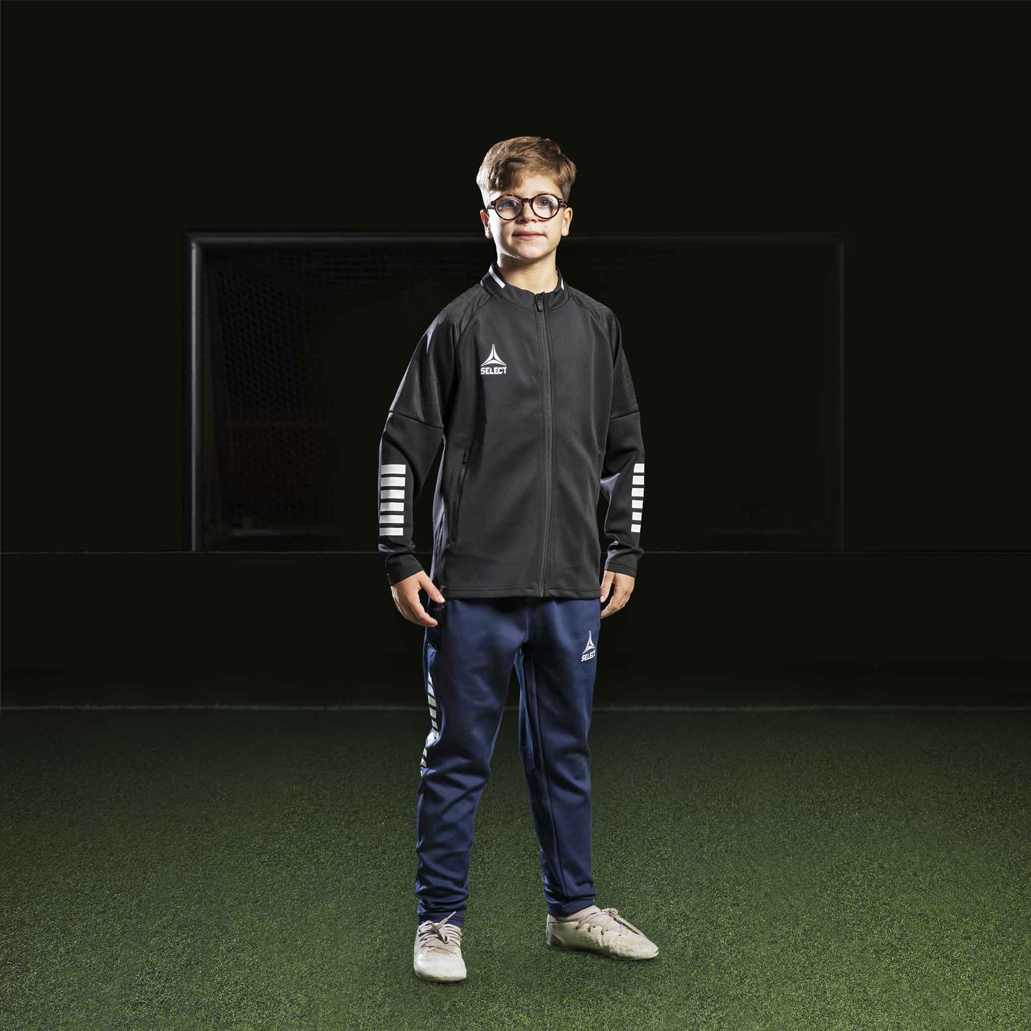 Gutt fotballspiller i sort Zip jacket Monaco v24 og marineblå bukser, Match & Training wear, forfra.