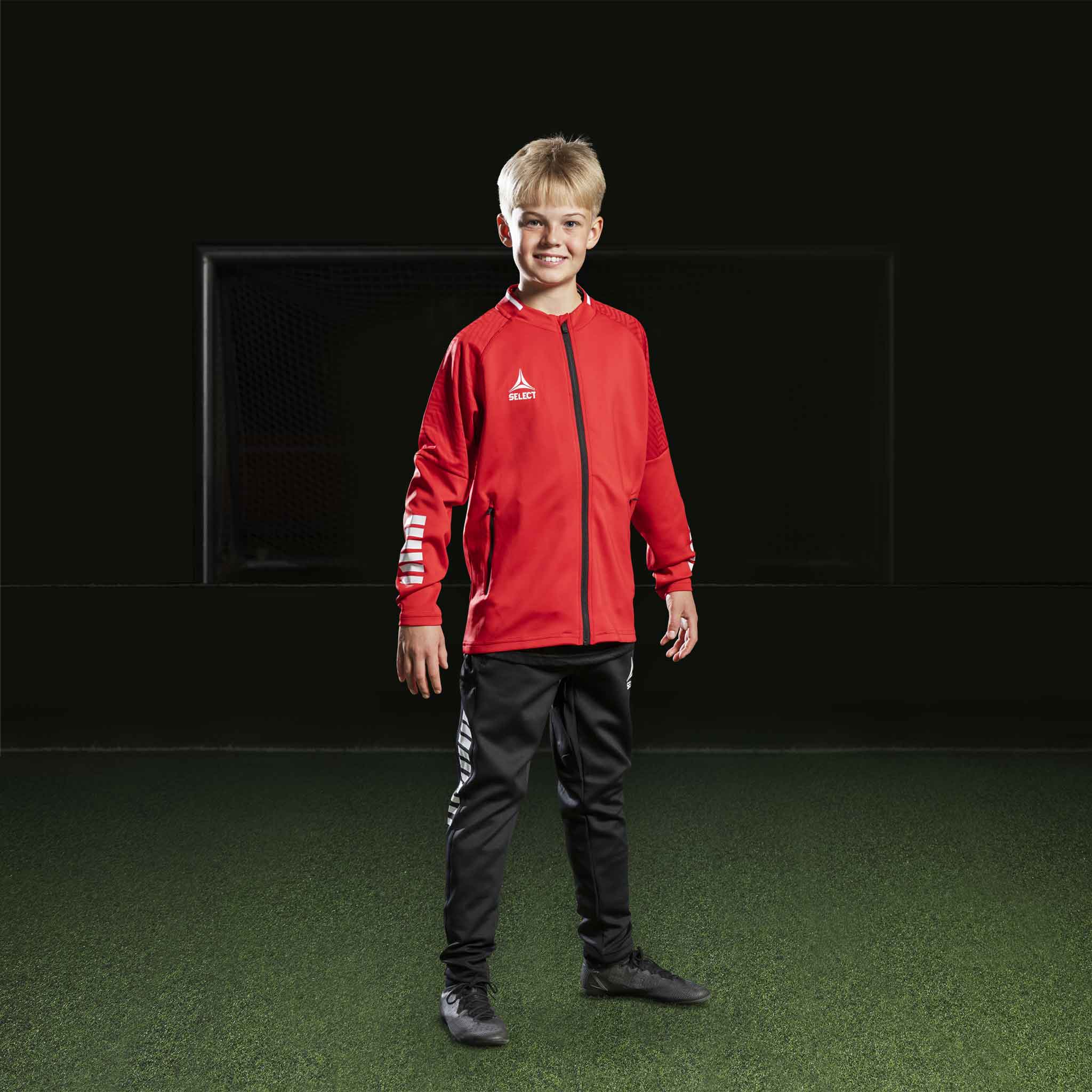 Gutt fotballspiller i rød Zip jacket Monaco v24 og svarte bukser, Match & Training wear, forfra.