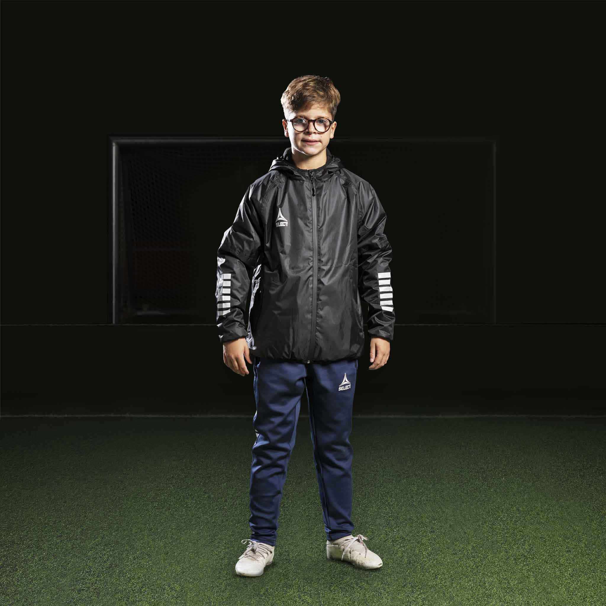 Dreng fodboldspiller i marineblå Training pants Regular Fit Monaco v24, sort jakke. Kamp- og træningstøj.