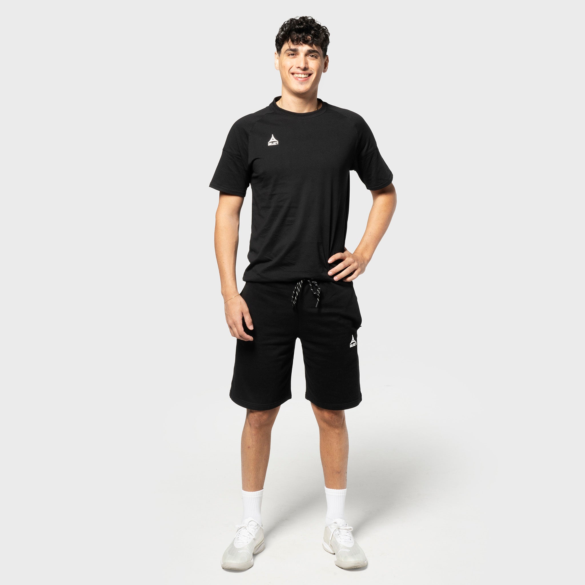 Mannlig fotballspiller i sorte Sweat shorts Oxford v25 og sort t-skjorte, fritidsklær, sett forfra.