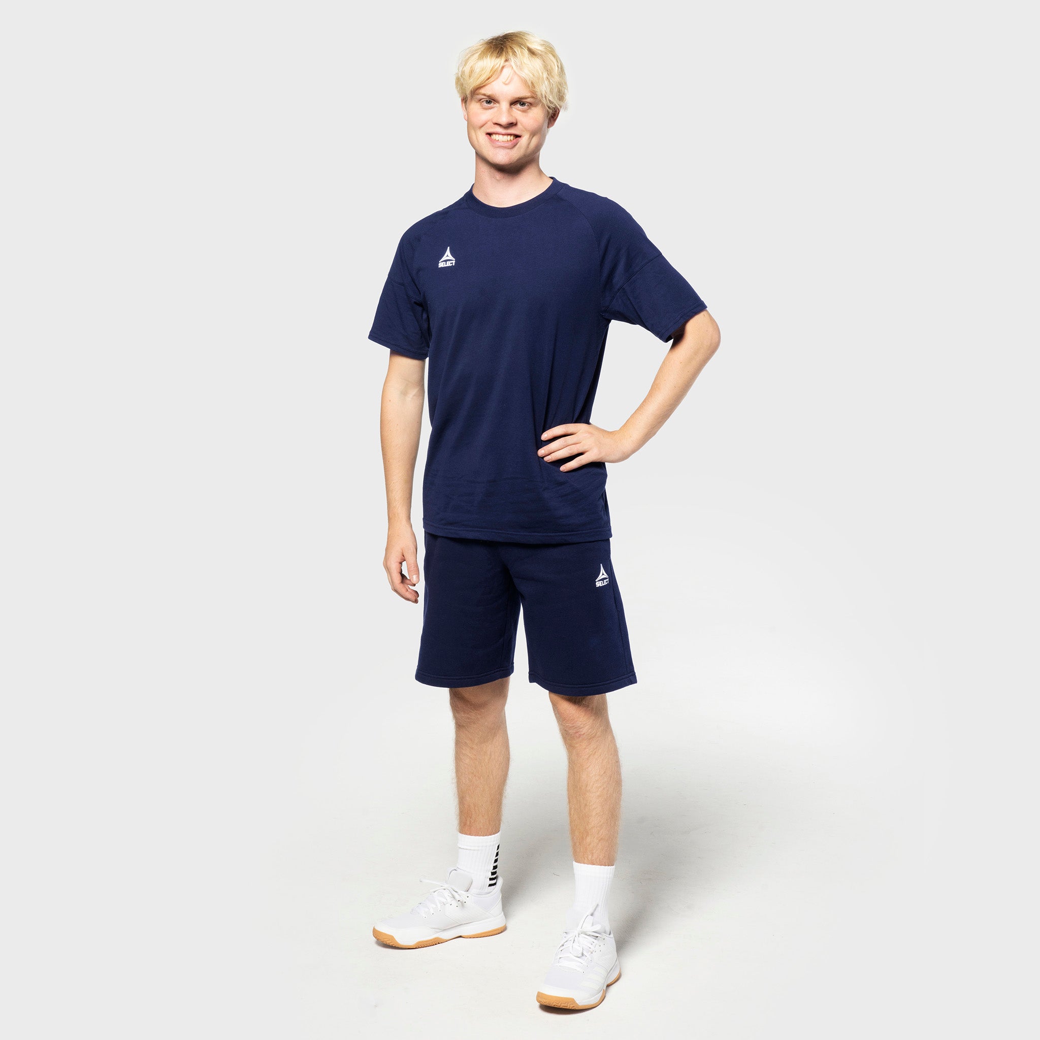 Mannlig fotballspiller i marineblå Sweat shorts Oxford v25 og marineblå t-skjorte, fritidsklær, sett forfra.