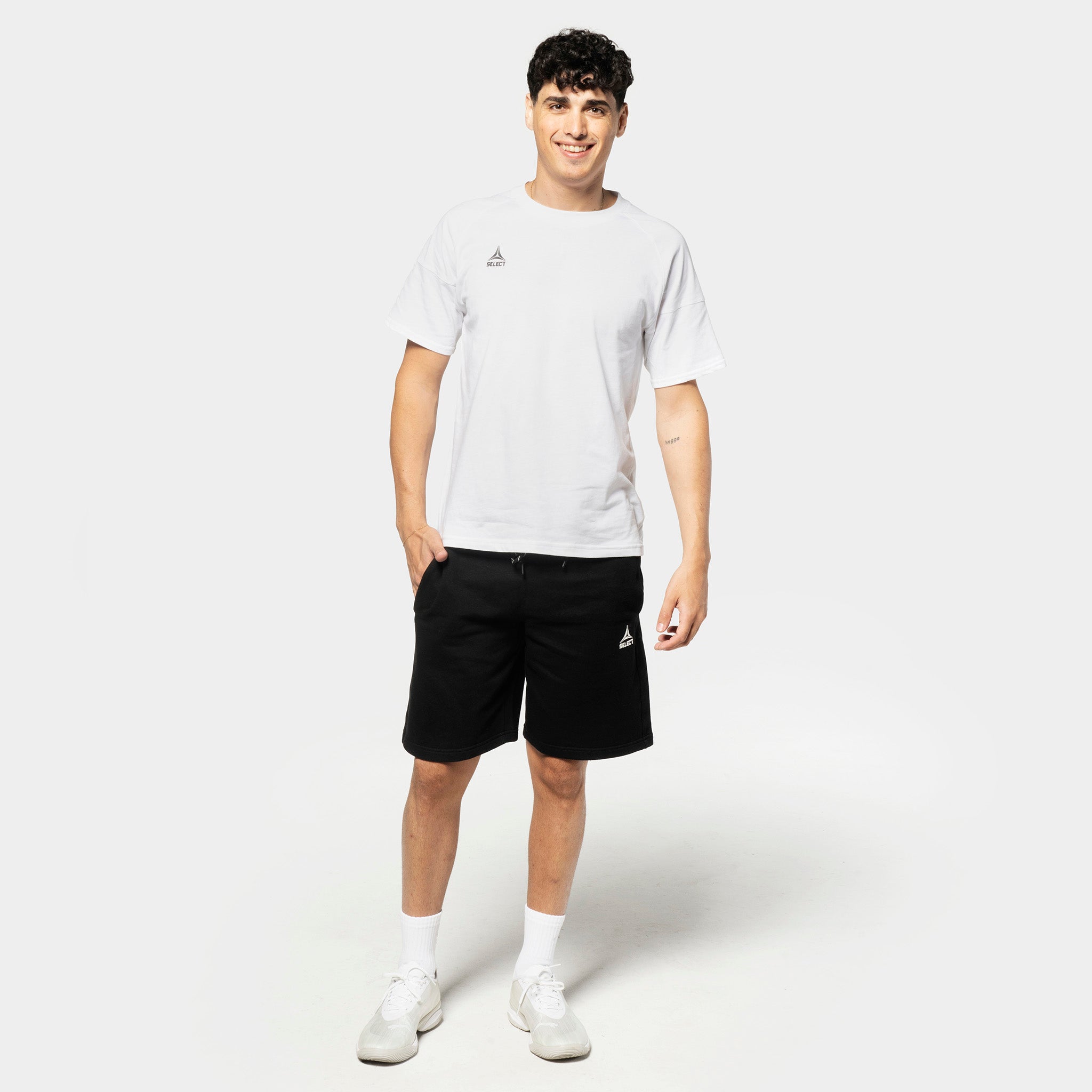 Mannlig fotballspiller i hvit t-skjorte og sorte Sweat shorts Oxford v25, fritidsklær, sett forfra.