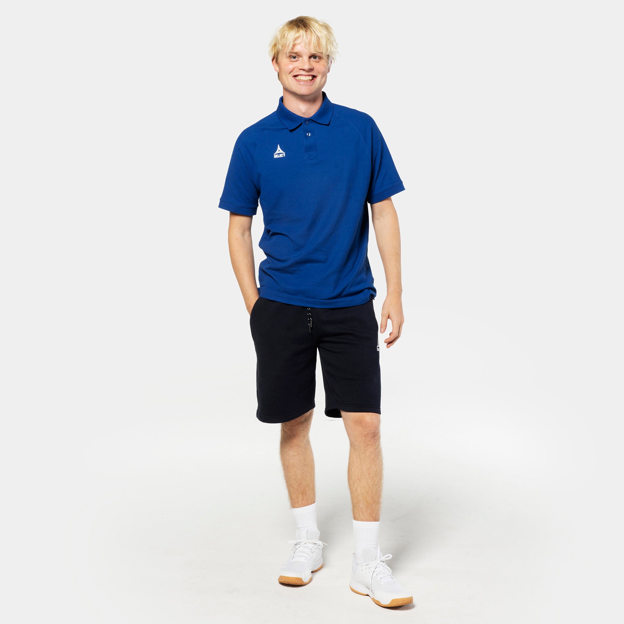 Mannlig fotballspiller i blå polo og svarte Sweat shorts Oxford v25, fritidsklær, forfra.