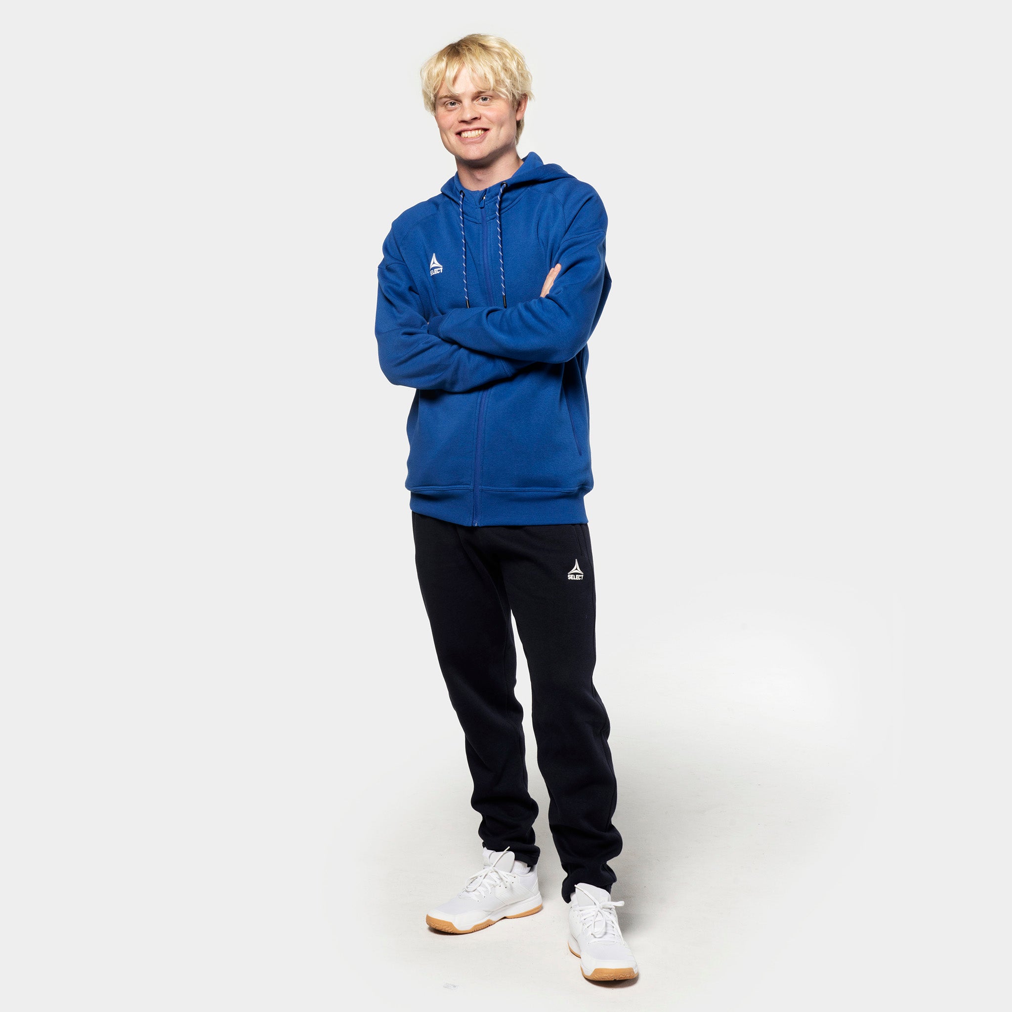 Mannlig fotballspiller i blå zip hoodie og svarte Sweat pants Oxford v25, fritidsklær, sett forfra.