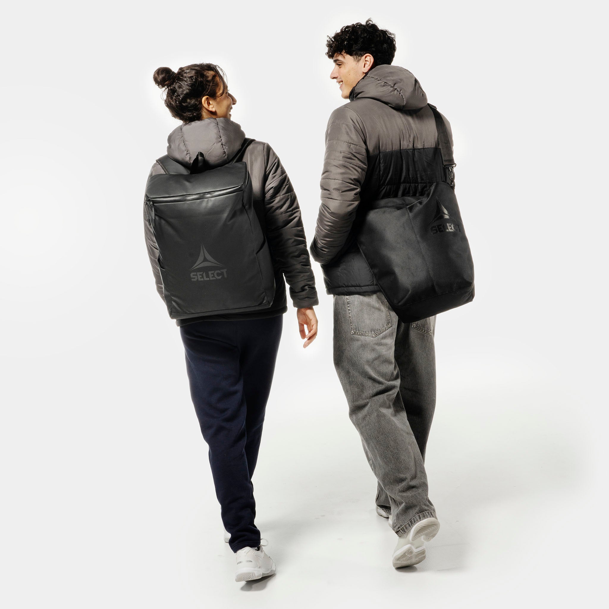 Kvinne og mann fotballspillere med sorte Crossbody v25 sportsbager, sett bakfra.