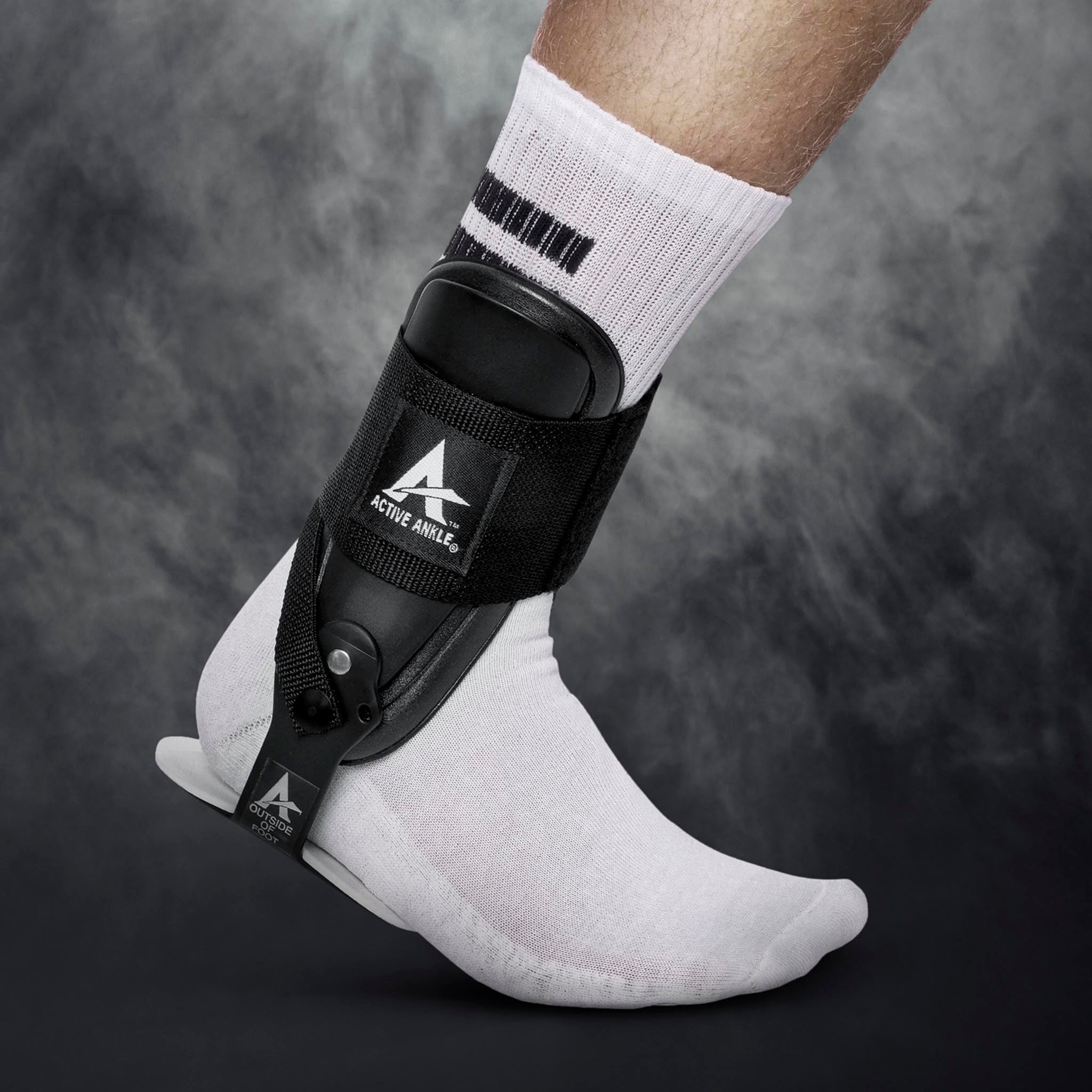 Svart Active Ankle T-2 sportsstøtte på en fotballspillers fot med hvit sokk, sett forfra