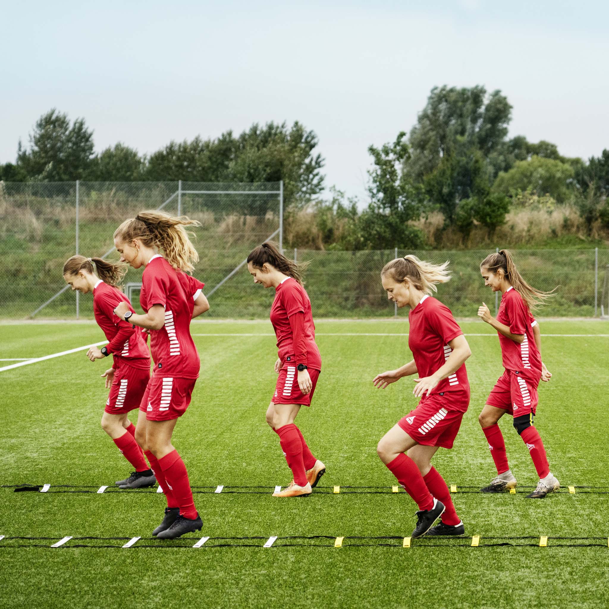 Kvinnelige fotballspillere trener med oransje og gul Agility ladder, fotball treningsutstyr, på grønn bane.