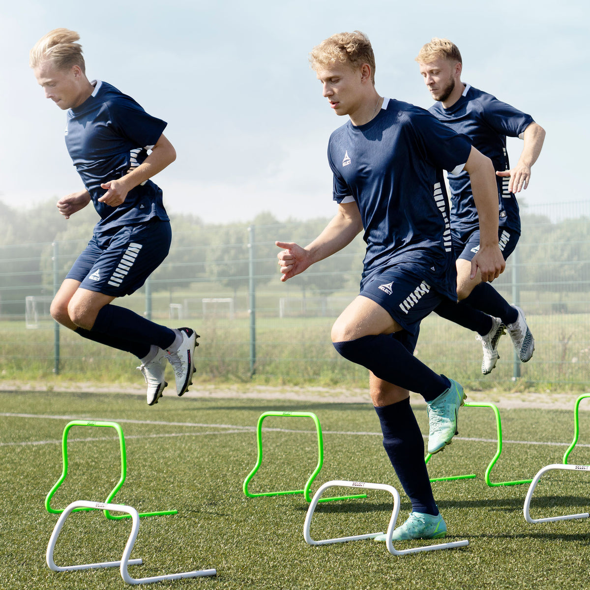 Fotballspillere trener over grønne Training hurdle på en bane. Treningsutstyr, actionbilde.